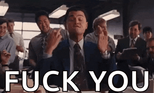 a man in a suit and tie is giving a middle finger in front of a group of people .