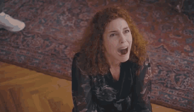 a woman with curly red hair is sitting on the floor eating something