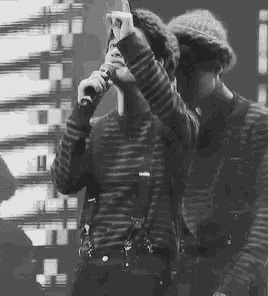a man is singing into a microphone while another man looks on .