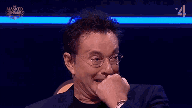 a man wearing glasses and a black suit is on a tv show called the masked singer