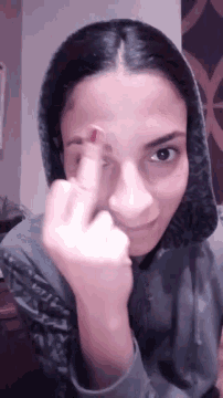 a woman wearing a grey hoodie is making a funny face with her middle finger