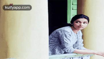 a woman is peeking out of a window and reaching out her hand .