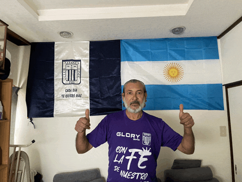 a man wearing a purple shirt that says glory con la fe de nuestro gives a thumbs up