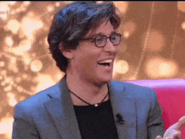 a man wearing glasses and a suit is laughing with his mouth open