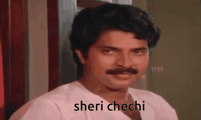 a man with a mustache is wearing a white shirt and the words sheri chechi are on his face .