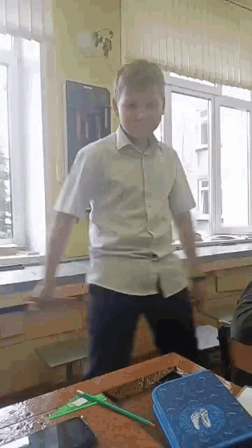 a boy in a white shirt is dancing in a classroom with a blue pencil case on the desk .