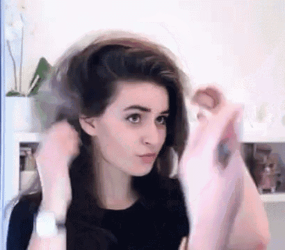 a woman is blow drying her hair in front of a mirror in a kitchen .