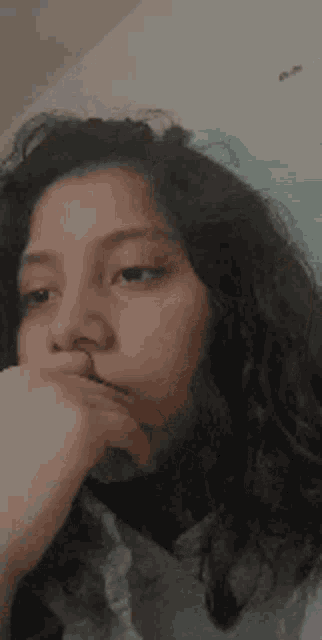 a close up of a girl with curly hair covering her mouth with her hand .