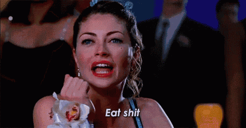 a woman is sitting at a table with a flower in her hand and says eat shit .