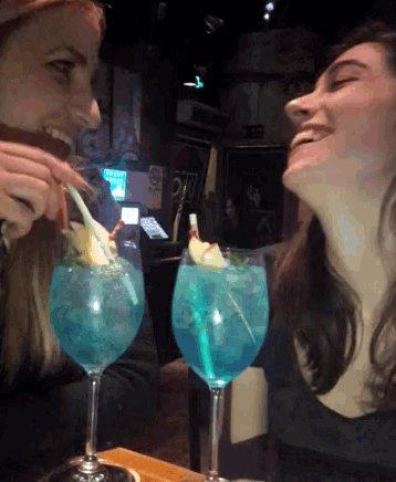 two women are sitting at a table with glasses of blue liquid in front of them