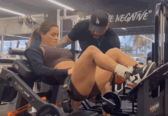 a man helps a woman lift weights in a gym with a sign that says " negative "