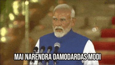 a man with a beard stands in front of a microphone and says mai narendra damodadas modi