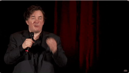 a man singing into a microphone with the word comedy on the bottom left