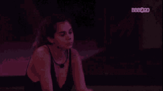 a woman in a black tank top is standing in a dark room with her arm outstretched .