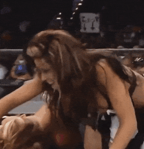two women are wrestling in a ring and one of them is laying on the other 's back .