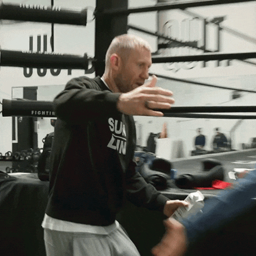 a man wearing a black sun lin sweatshirt stands in a boxing ring