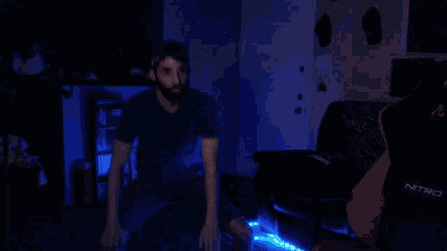 a man is dancing in a dark room with a chair that says nzxt on it