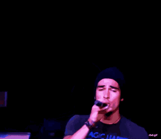 a man singing into a microphone while wearing a hat