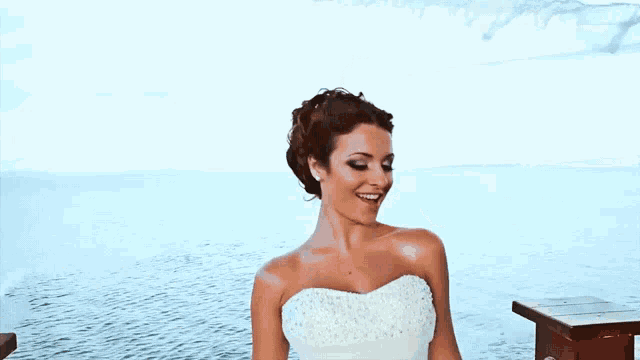 a woman in a white wedding dress is dancing in front of the ocean