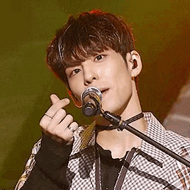 a young man is singing into a microphone and making a heart with his hands .