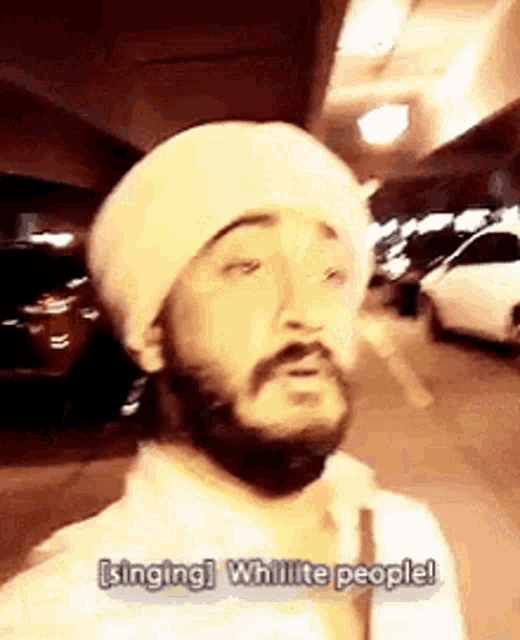 a man with a beard wearing a white hat is singing while talking to people .