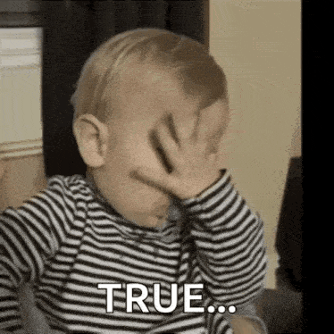 a baby is covering his face with his hand and saying true .