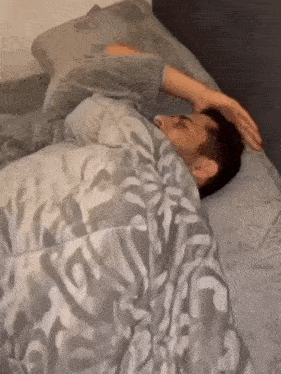 a man is sleeping in a bed with a blanket on top of him .