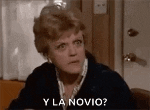 a woman is sitting at a table with a door in the background and asking y la novia .