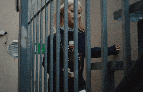 a woman is behind bars with a green exit sign behind her