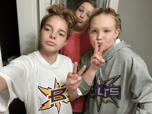 three young girls are posing for a picture and one has a shirt that says lts