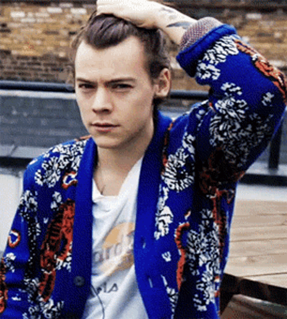 a young man with a tattoo on his arm is wearing a blue jacket and a white shirt that says ' harry ' on it