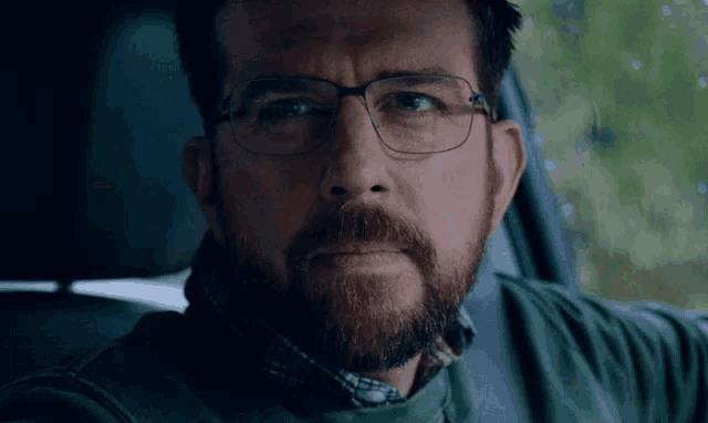 a man with glasses and a beard is sitting in the back seat of a car .