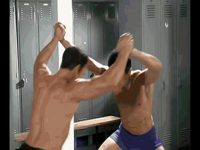 two shirtless men are wrestling in a locker room with lockers in the background