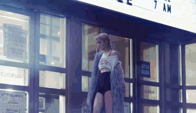a woman in a fur coat is standing in front of a building that says 7 am