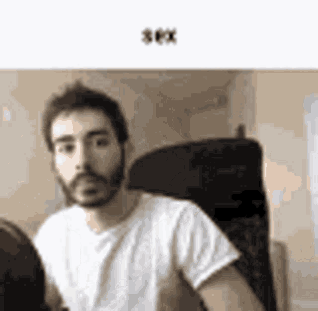 a man with a beard is sitting in a chair looking at the camera .