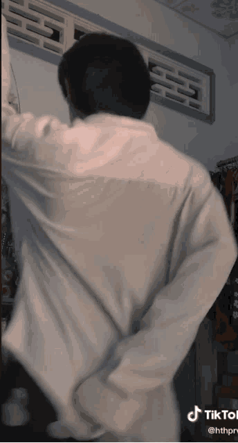 a man in a white shirt is standing in front of a window with tiktok written on the bottom right