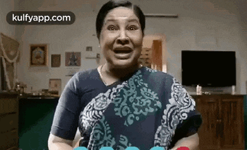 a woman in a saree is making a funny face while holding a cake in a living room .
