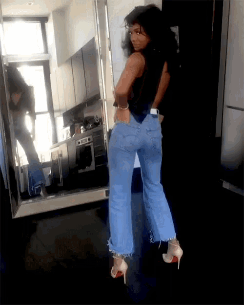 a woman in jeans and heels is standing in front of a mirror in a kitchen