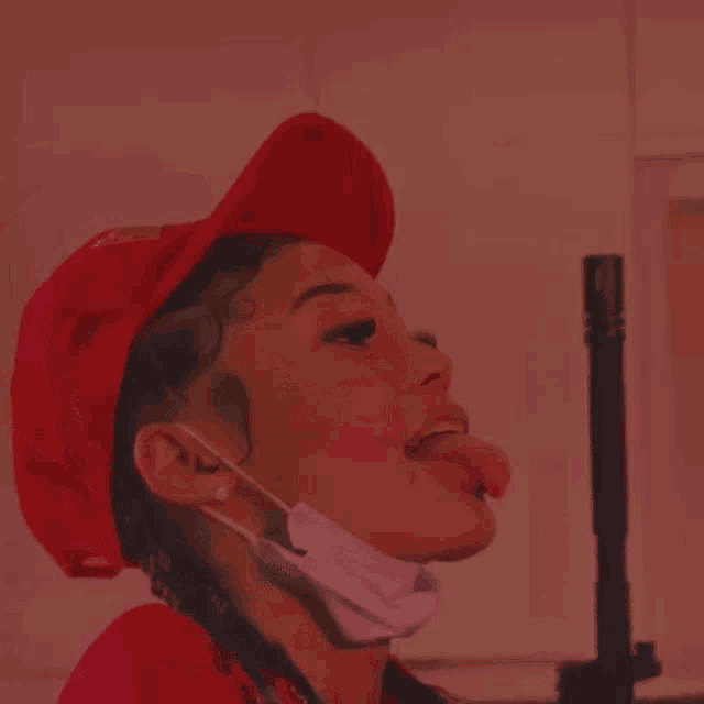 a woman wearing a red hat and a surgical mask is sticking her tongue out .