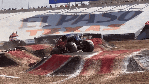 a monster truck races down a dirt track in front of a el paso texas sign