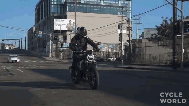 a man riding a motorcycle on a city street with cycle world written on the bottom right