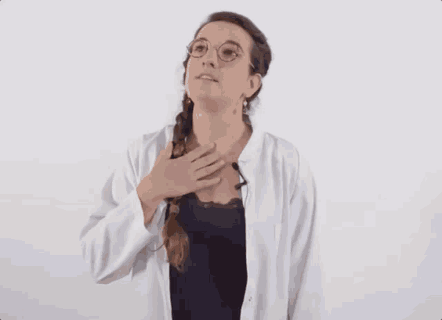 a woman wearing glasses and a lab coat laughs with her hand on her chest
