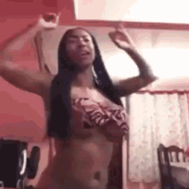 a woman in a bikini is dancing in a room with her arms in the air .