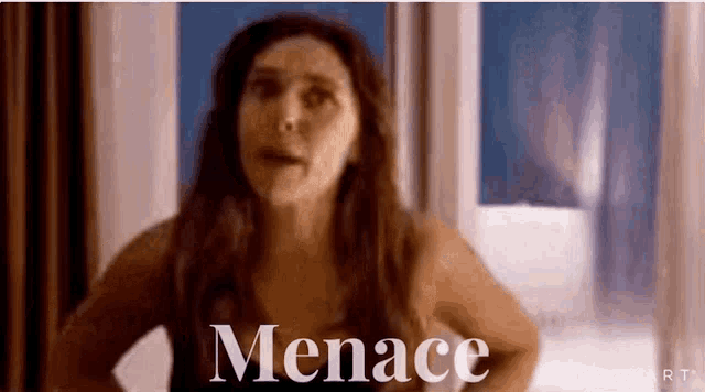 a woman is standing in front of a window with the word menace written on the bottom of her face .