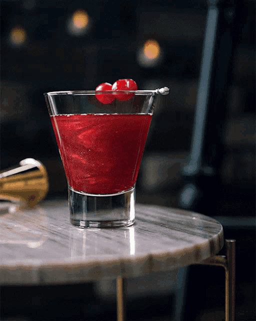 a glass of red liquid with a cherry on top of it
