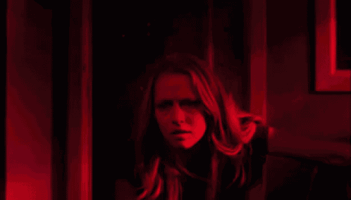 a woman is standing in a dark room with a red light behind her .