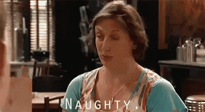 a woman in a blue shirt is sitting at a table with the word naughty written on it .