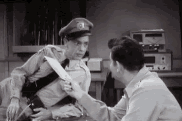 a man in a police uniform is holding a knife while another man holds a piece of paper .