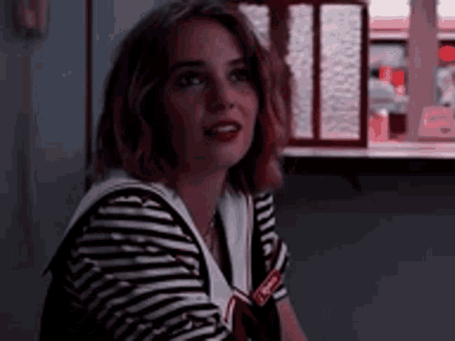a woman wearing a striped shirt and a sailor outfit is sitting in front of a window .