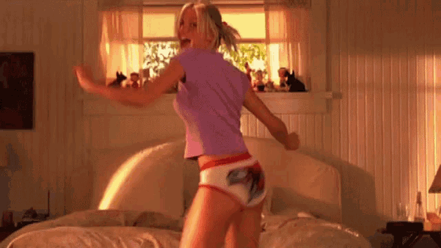 a woman is dancing in a bedroom in front of a bed .
